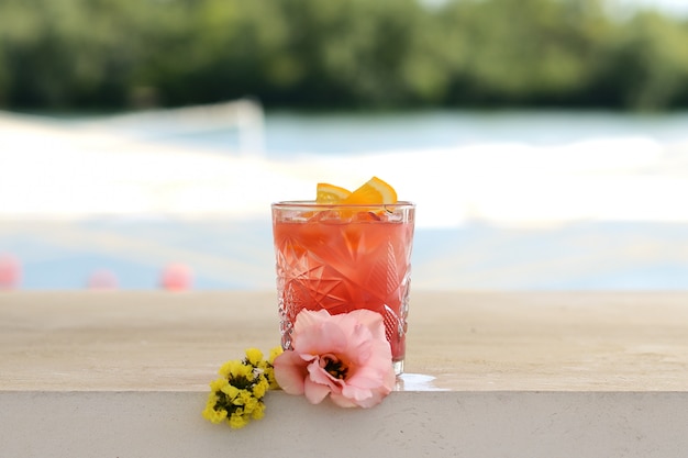 Cocktail rosso in un bicchiere con una fetta di arancia. Con decorazioni floreali