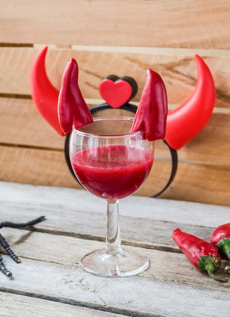Cocktail rosso per la celebrazione di Halloween decorato con peperoncini con corna da diavolo. Sulla superficie in legno