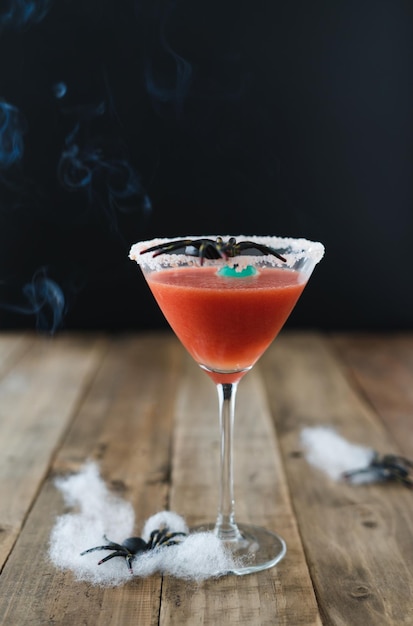 Cocktail rosso terrificante con ragno su sfondo nero e tavolo di Halloween in legno con decorazione verticale