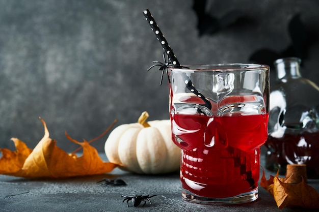 Cocktail sanguinante di Halloween Calice da cocktail rosso sanguinante per Halloween e bottiglia a forma di teschio su sfondi scuri Festa di Halloween con occhi caramellati pipistrelli ragni Dia de los muertos Clousup