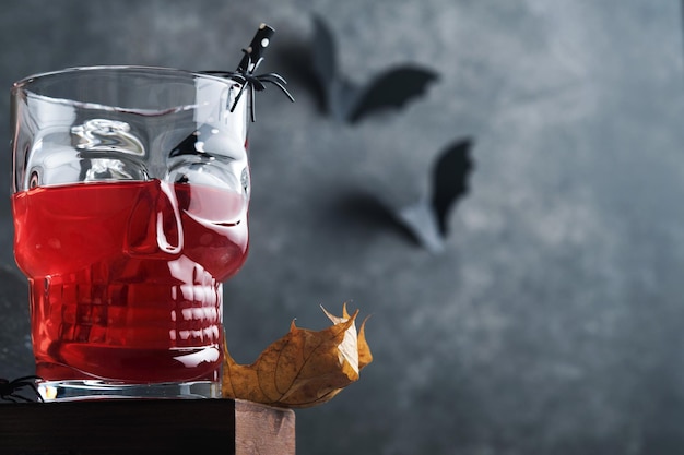 Cocktail sanguinante di Halloween Calice da cocktail rosso sanguinante per Halloween e bottiglia a forma di teschio su sfondi scuri Festa di Halloween con occhi caramellati pipistrelli ragni Dia de los muertos Clousup