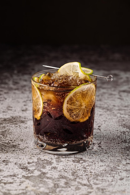 Cocktail scuro con cola e arance su sfondo nero