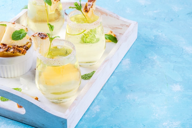 Cocktail tropicale della margarita del succo di ananas con il vassoio di legno del fondo blu-chiaro della menta fresca