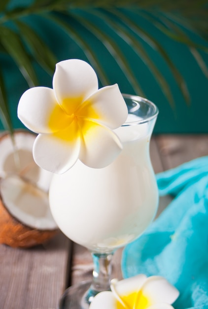 Cocktail tropicale esotico caraibico bevanda pina colada in bicchieri con fiori di plumeria frangipani, foglia di palma e cocco sullo sfondo. Concetto di picnic spiaggia tropicale.