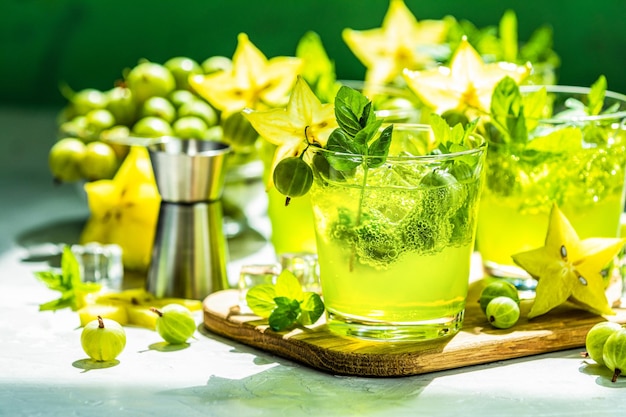 Cocktail verde di uva spina e carambola con ghiaccio al liquore e menta fresca su un tavolo di cemento grigio chiaro Bevanda estiva rinfrescante, luce soleggiata o bevanda disintossicante