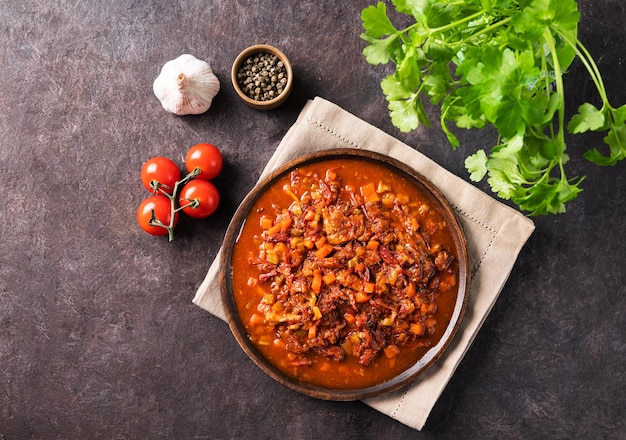 Coda di bue in umido con verdure in un piatto di legno su uno sfondo scuro con pomodori freschi pepe ed erbe aromatiche Stufato di carne Il concetto di cucina tradizionale spagnola