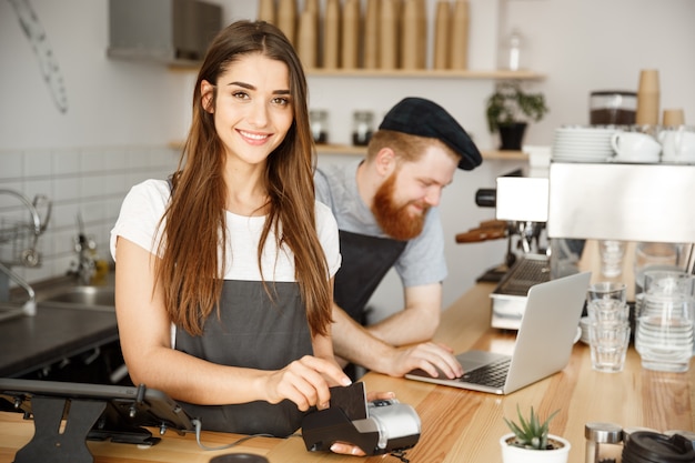 Coffee Business Concept - Bella barista femminile che dà servizio di pagamento per il cliente con carta di credito e sorridente, mentre lavora al banco bar nel moderno negozio di caffè.