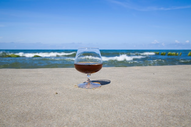 Cognac in un bicchiere sulla riva del mare blu. Resta con l'alcol al Sud