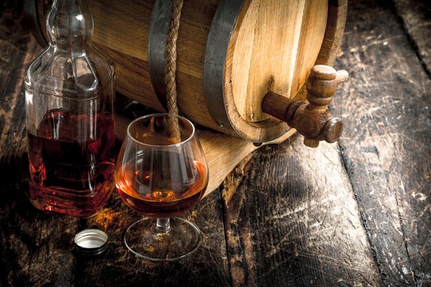 Cognac in una botte con un bicchiere. Su uno sfondo di legno.