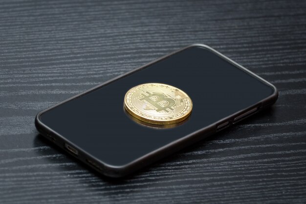 Coin criptovaluta Bitcoin al telefono. Tavolo in legno nero