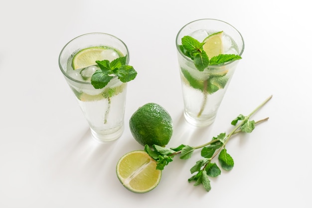 Coktail Gin Tonic o Mojito in vetro con menta, ghiaccio, lime su fondo bianco.