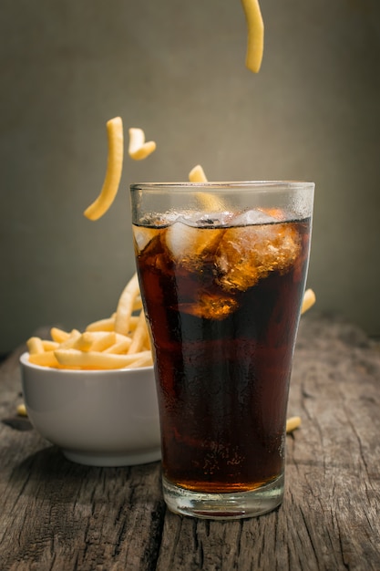 Cola con cubetti di ghiaccio Posizionato sul tavolo di legno con sfondo di patatine fritte.
