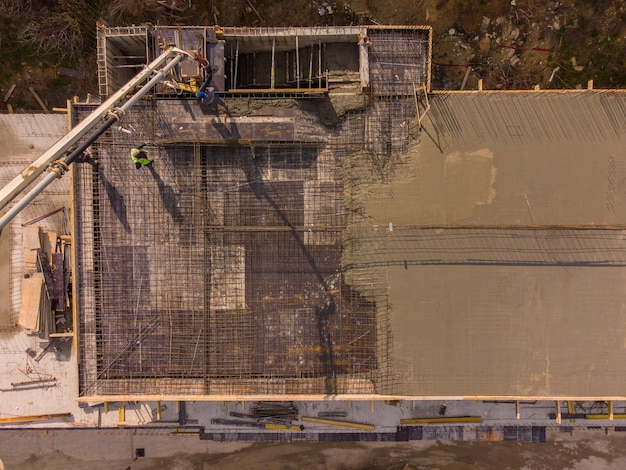 Colata di cemento cementizio sul tetto di un edificio residenziale in costruzione utilizzando una macchina autocarro con pompa per calcestruzzo con braccio alto per fornire la miscela ai piani superiori Vista aerea