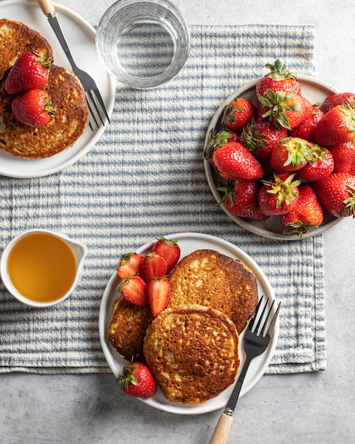 Colazione a base di frittelle con fragole e miele su una tovaglia a righe Vista dall'alto