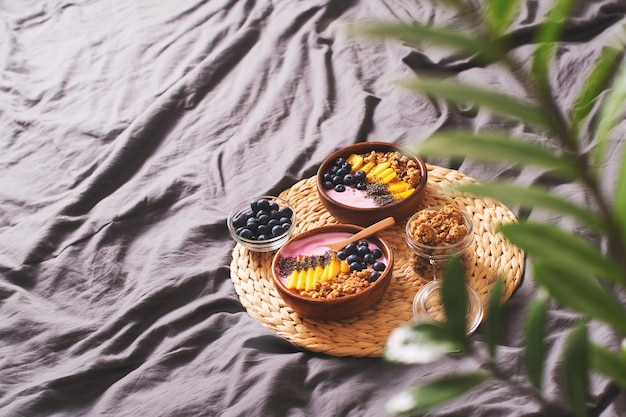 Colazione a letto con ciotola per frullati con muesli, mango, yogurt e mirtillo su sfondo grigio