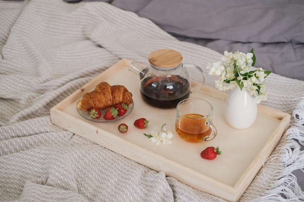 Colazione a letto Vassoio con croissant al tè e fragole sul letto in camera da letto