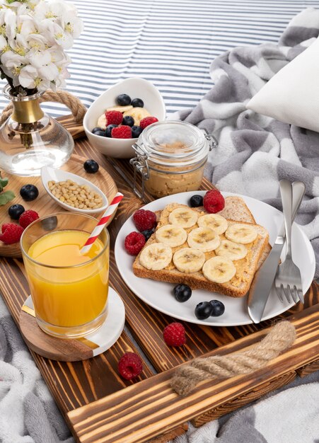 Colazione a letto. Vassoio in legno con bicchiere di succo d'arancia e sandwich con frutti di bosco