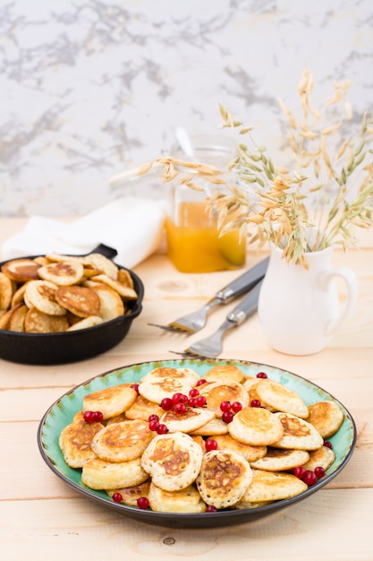 Colazione alla moda. Mini pancake olandesi con ribes rosso su un piatto e una padella con loro su un tavolo di legno.