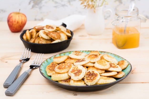 Colazione alla moda. Mini pancake olandesi su un piatto e una padella con loro su una tavola di legno.