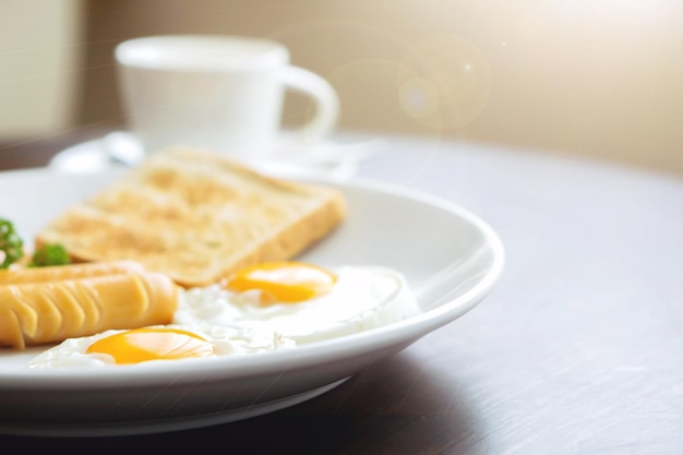 Colazione americana e caffè caldo in una tazza di caffè in ceramica bianca su un tavolo di legno con caldo sole mattutino e sfondo riflesso lente.