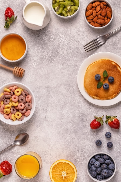 Colazione con anelli di cereali colorati, frittelle, frutta, latte, succo di frutta