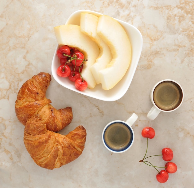 Colazione con caffè, cornetti e frutta - melone, fragole, ciliegie