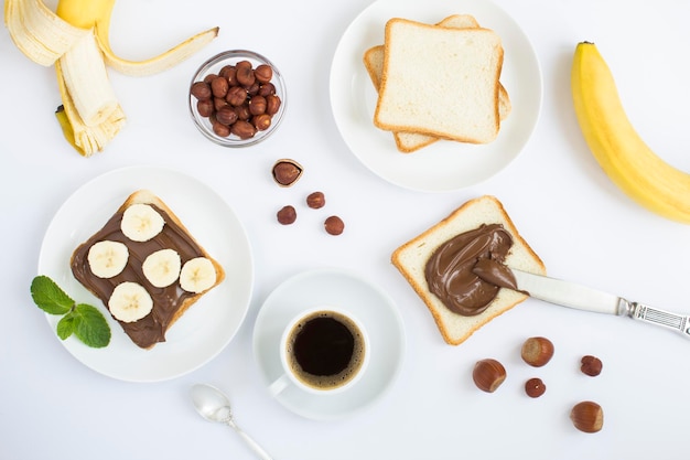 Colazione con crema di cioccolato, pane, banana e caffè su sfondo bianco Vista dall'alto