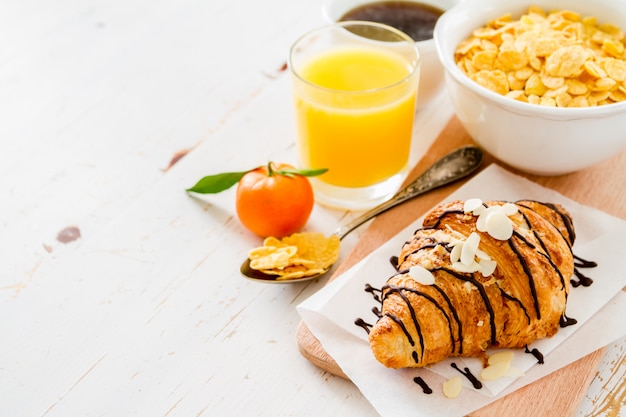 Colazione con croissant, succo di frutta, caffè e cereali