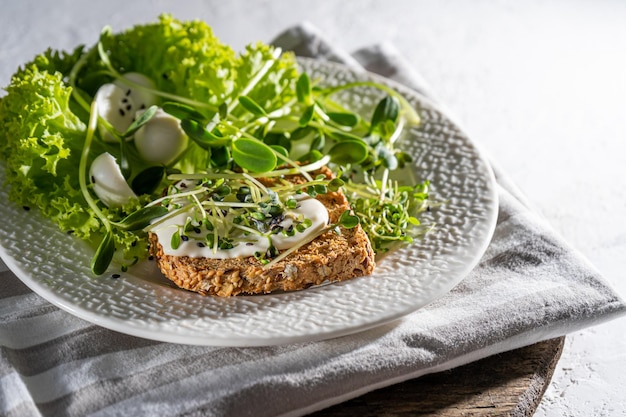 Colazione con microgreen su un piatto Pane tostato mozzarella salsa cremosa Cibo con germogli verdi di micro green Dieta sana Cibo semplice Insalata con germogli di girasole rucola ravanello senape