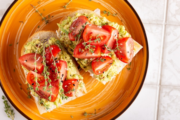 Colazione con panini vegetariani con avocado e pomodori su un grande piatto arancione