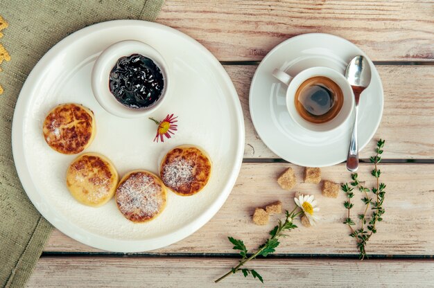 Colazione con quattro frittelle di formaggio, caffè nero e marmellata di ribes