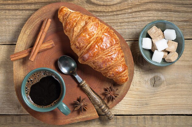 Colazione con tazza di caffè, croissant e spezie disposti su un tavolo di legno, vista dall'alto