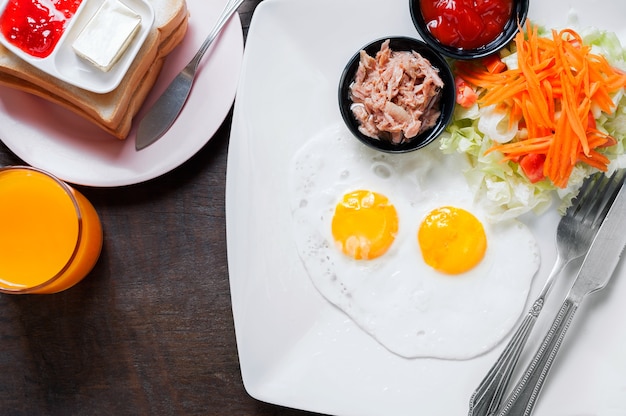 Colazione con uova fritte, salsicce, fette di pane con marmellata di fragole