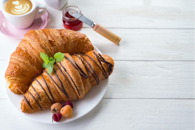 Colazione continentale croissant appena sfornato decorato con marmellata e cioccolato