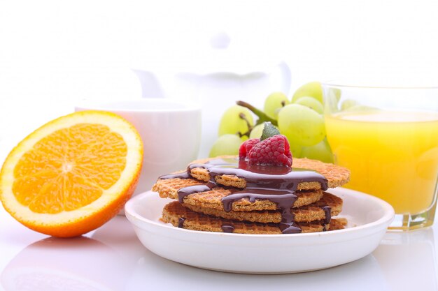 Colazione del fine settimana: cialde con cioccolato e lamponi, uva, tè e succo d&#39;arancia