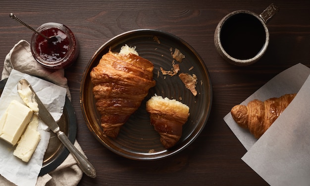 Colazione del mattino con cornetto e fetta sul piatto, tazza di caffè, marmellata e burro.