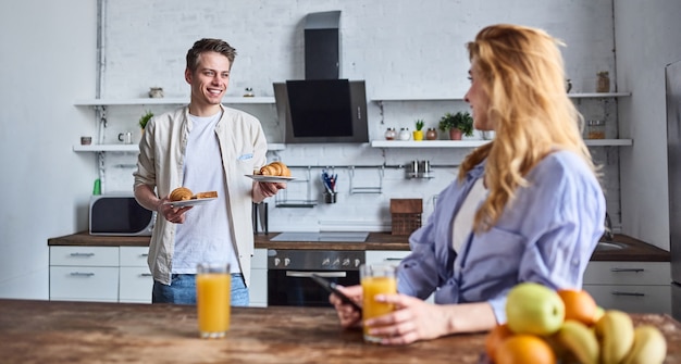 Colazione di una giovane coppia innamorata nella cucina di casa. La bella ragazza con un telefono in mano beve il succo. Colazione preparata dal fidanzato.