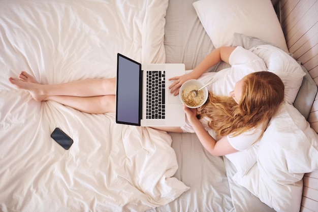 Colazione e wifi ciò che amo Inquadratura di una giovane donna che fa colazione e usa un laptop a casa