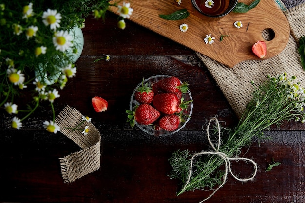 Colazione estiva naturale Fragole fresche fiori di camomilla tè naturale e menta su tavola di legno Stile di vita estivo estetico Cibo bellissimo Collegamento con la natura