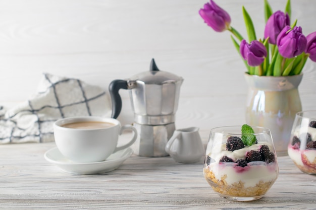 Colazione fresca e salutare con muesli, yogurt, caffè e bouquet di tulipani viola