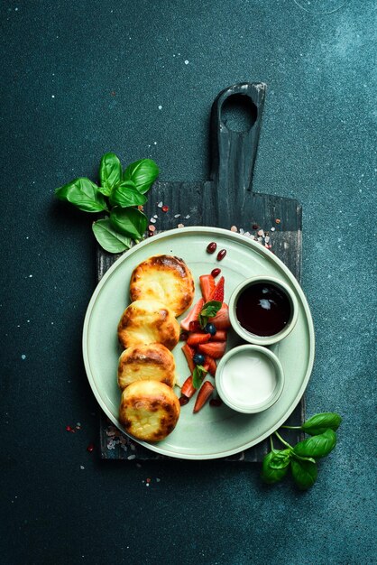 Colazione Frittelle di formaggio con panna acida e frutta su un piatto Su uno sfondo di pietra nera