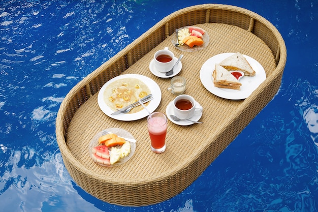 Colazione galleggiante in piscina. Vassoio di paglia con cibo diverso.