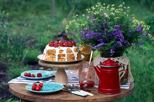 Colazione in giardino. sul tavolo c'è un vaso di fiori, una torta con le fragole e bicchieri di limonata