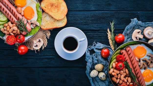 Colazione inglese completa con uova fritte, salsicce, fagioli, toast e caffè su sfondo copia spazio su uno sfondo di legno nero