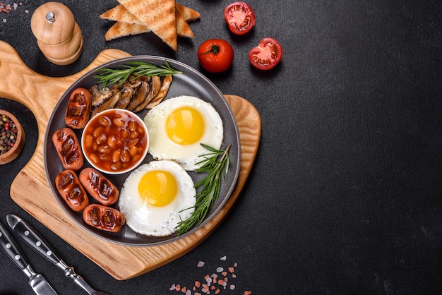 Colazione inglese completa fagioli uova fritte salsicce arrostite pomodori funghi su un tavolo di cemento scuro con pane tostato