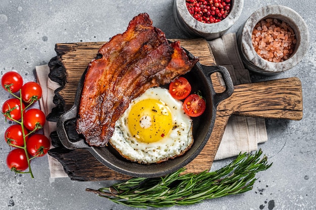 Colazione inglese con uova fritte e pancetta in padella di ghisa Sfondo grigio Vista dall'alto