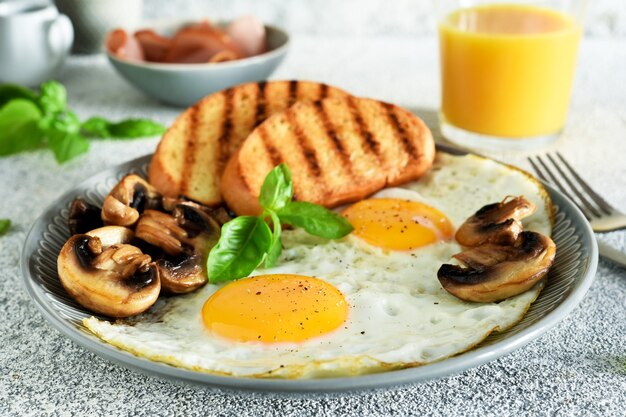 Colazione inglese. Uova fritte con funghi e prosciutto con un bicchiere di succo d'arancia per colazione. Buongiorno.