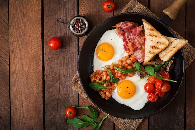 Colazione inglese - uova fritte, fagioli, pomodori, funghi, pancetta e pane tostato