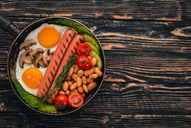 Colazione inglese uova fritte fagioli pomodori funghi pancetta e toast Vista dall'alto su uno sfondo di legno