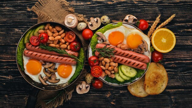 Colazione inglese uova fritte fagioli pomodori funghi pancetta e toast Vista dall'alto su uno sfondo di legno